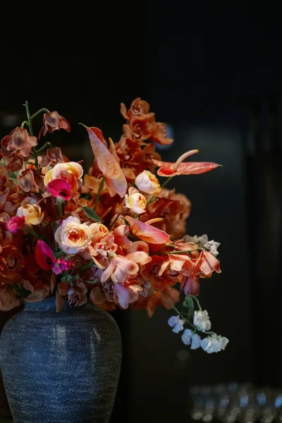 Wedding floral arrangement with orchids and anthurium in a ceramic vase, featuring roses and greenery against a dark backdrop