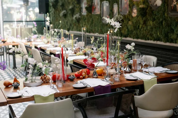 Reception tablescape with long banquet table wedding styling, scalloped placemats, taper candles, anthuriums, and fruit before a green moss wall