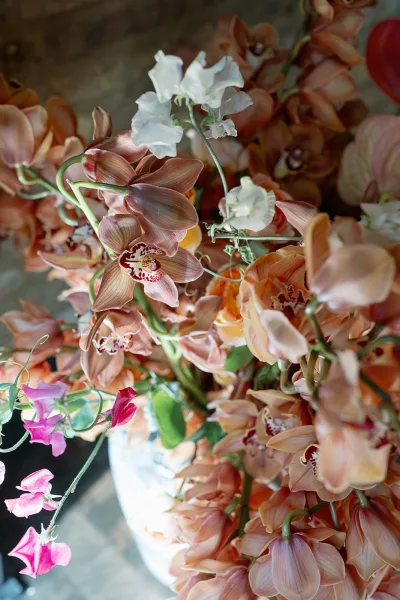 Wedding flowers with orchid wedding flowers in a vase, featuring sweet peas arranged on a stone floor for a modern, pastel centerpiece