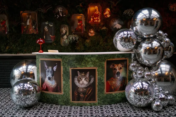 Wedding welcome table with silver balloon garland and disco balls, framed pet portraits, and moss wall backdrop on patterned tile floor indoors