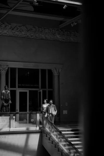 Couple portrait in black and white, bride in strapless dress and groom in light suit on a museum staircase by columns and statue