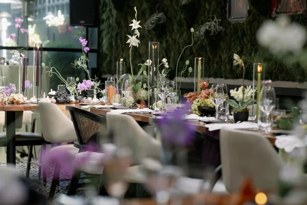 Reception tablescape on a long table wedding reception with taper candles, orchids, grapes, and garlic place settings against a greenery wall