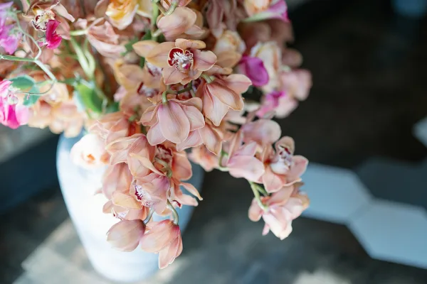 Orchid arrangement wedding orchid centerpiece of pink and peach blooms in a ceramic vase on a dark tabletop with soft-focus interior background