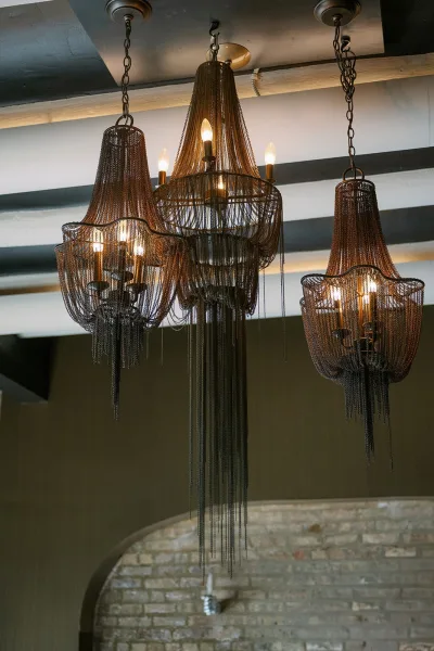 Chandelier lighting with hanging chain chandeliers and candle-style bulbs, clustered beneath ceiling beams and a brick wall arch