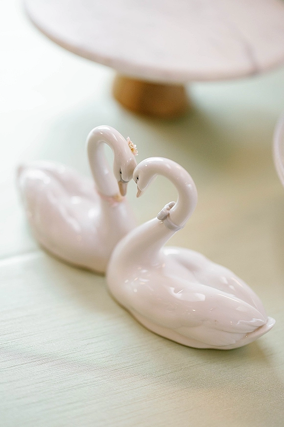 Wedding cake topper with swan cake topper figurines, delicate floral detail, displayed on a cake stand atop a table surface