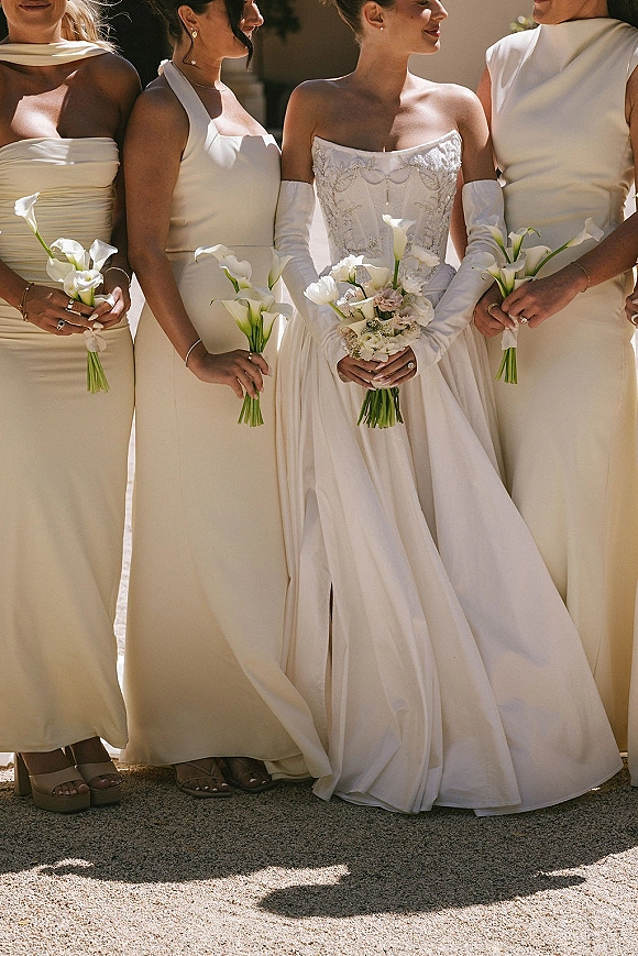 Bridesmaid portrait of the bride with bridesmaids in white and cream dresses holding calla lily bouquets on a sunlit walkway with shadows