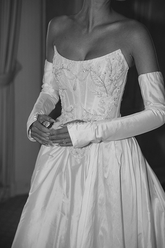 Wedding dress close-up showing a strapless corset wedding dress with beaded bodice, opera gloves, engagement ring, and draped fabric backdrop