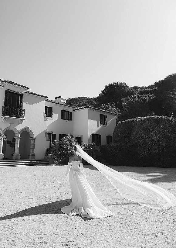 Bridal portrait from behind of a bride in a strapless gown with long veil and train flowing across a villa courtyard by an arched doorway