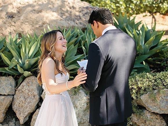 First look moment as bride in a strapless wedding dress touches groom’s shoulder while he reads vow letters in a sunlit succulent garden