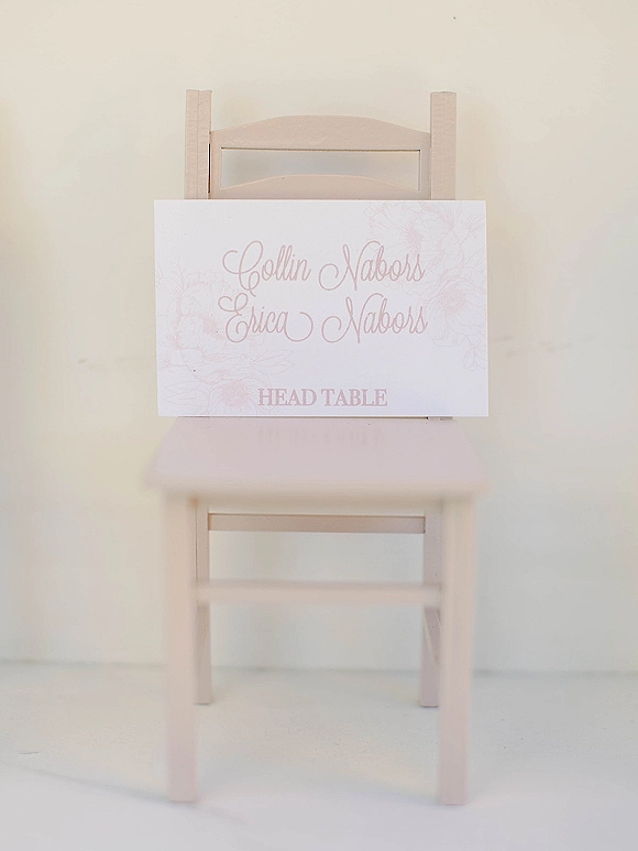 Wedding chair sign with paper calligraphy lettering tied to a wooden chair, set against a clean white wall and floor backdrop