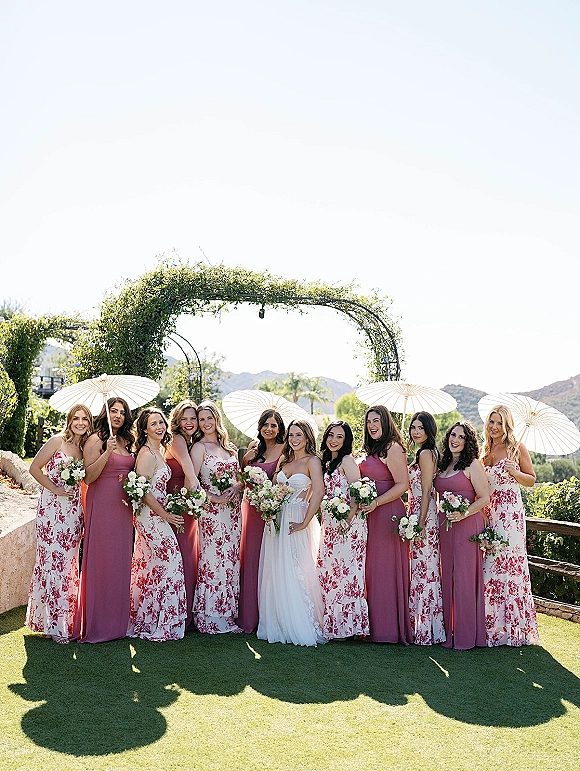 Bridesmaid group photo with bride and bridesmaids holding parasols, in mismatched dresses with bouquets on a lawn with mountain views