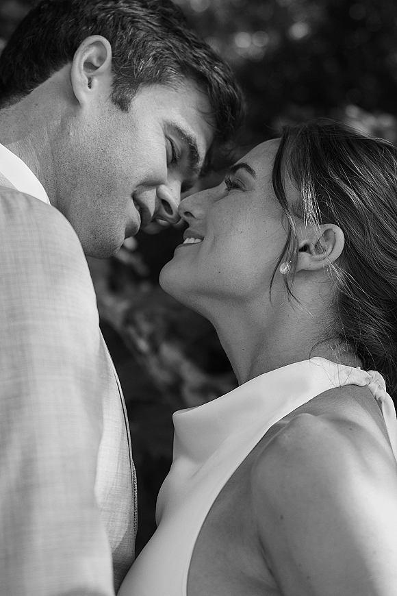 Wedding couple portrait of bride and groom in a wedding close up portrait, foreheads touching, bride in satin gown with pearl earrings in greenery