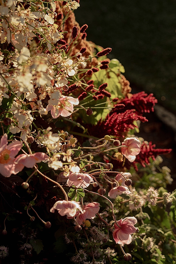 Wedding florals in a ceremony floral installation with pink and burgundy blooms and lush greenery against dark garden foliage backdrop