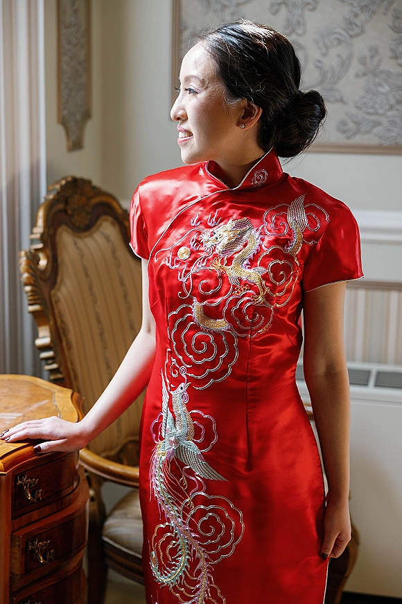 Bride portrait in a red qipao wedding dress with phoenix embroidery and mandarin collar, seated by window light on an ornate chair