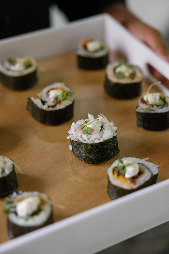 Wedding sushi catering displayed as sushi rolls on a wooden serving board, garnished with microgreens on a white tray in neutral indoor light