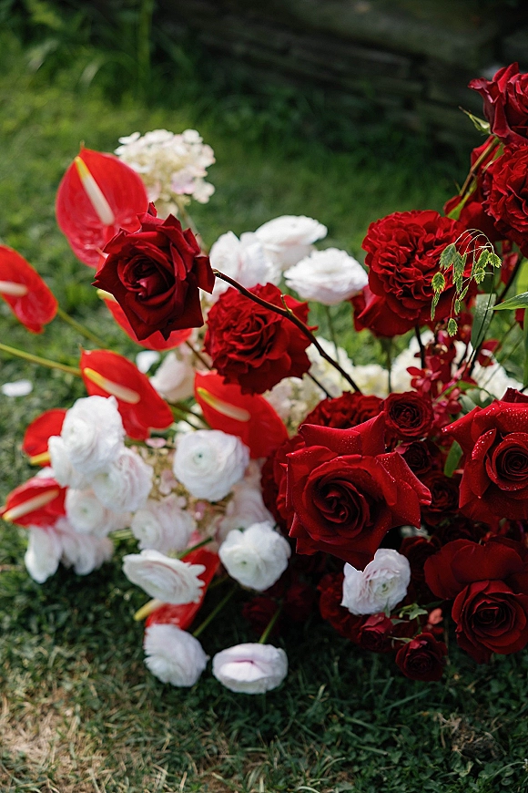 Wedding florals with red and white wedding flowers, featuring red roses and anthurium with greenery, arranged on a garden lawn