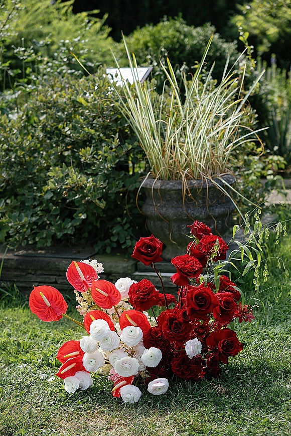Ceremony floral arrangement with red and white wedding flowers, red roses and anthurium in a stone planter by garden steps and lawn grass