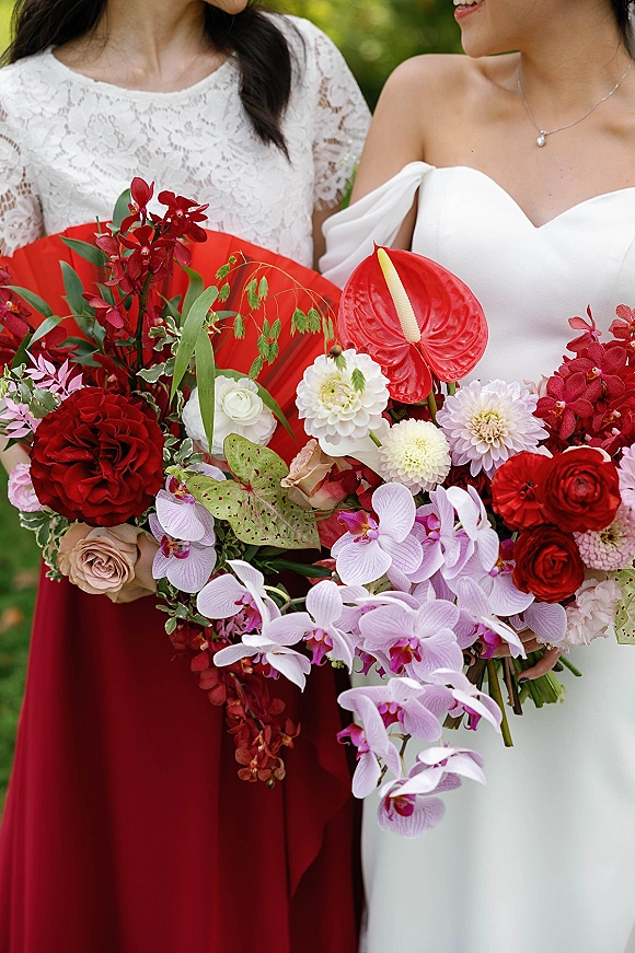 Wedding bouquet with a cascading orchid bouquet of red and white orchids, anthurium, roses and greenery, held against blurred garden foliage