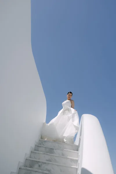 Bridal portrait of a bride on staircase, posed on a marble staircase framed by white walls and blue sky, wearing a bridal gown.