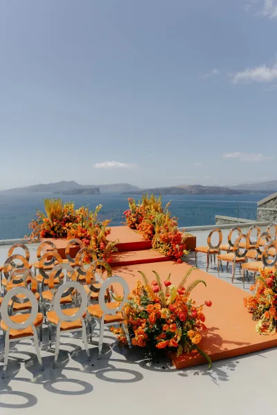 Ceremony setup for an orange wedding ceremony with a stepped aisle platform on a terrace overlooking the ocean and distant islands.