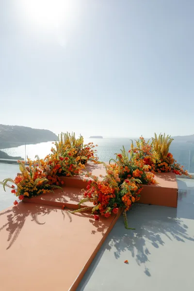 Ceremony setup showcasing outdoor ceremony decor with colorful florals, set against ocean cliffs beyond a sleek glass railing.