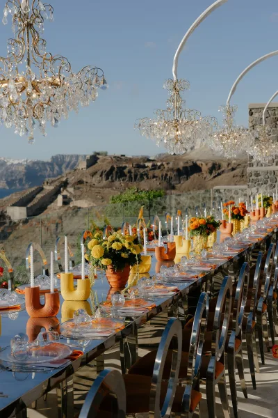 Reception tablescape styled for outdoor reception decor, with yellow and orange florals, set against a cliffside landscape and blue sky.