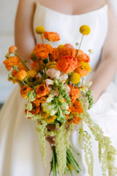 Bridal bouquet showcasing an orange wedding bouquet with ranunculus, arranged in a loose, organic cluster of bright yellow and orange blooms.