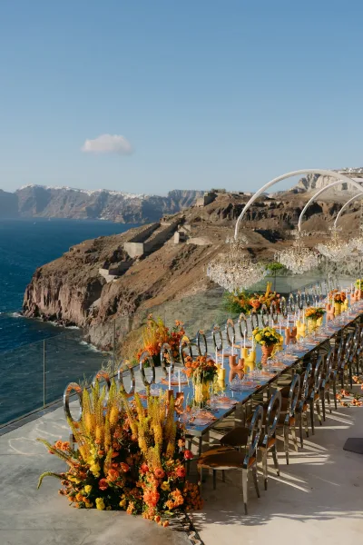 Reception tablescape with taper candles on an outdoor reception table, overlooking an ocean view with rocky cliffs and blue sky.