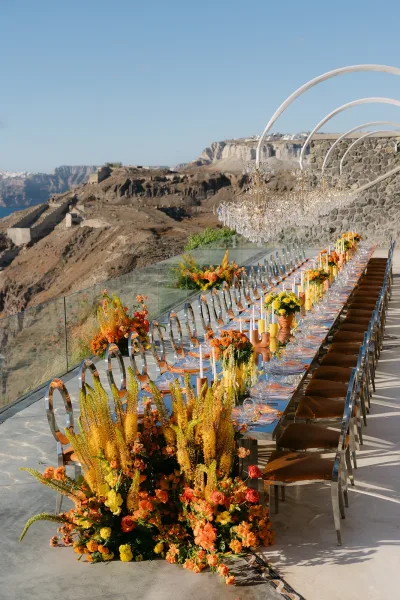 Reception tablescape with long banquet table decor featuring terracotta vases, set on a cliffside terrace with ocean view.