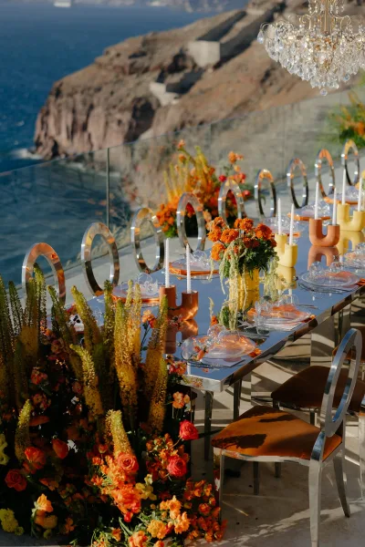 Reception tablescape on a mirrored wedding table with yellow taper candles, overlooking the ocean and coastal cliffs behind glass railing.