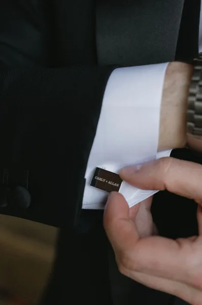 Groom cufflinks being fastened on a white dress shirt, with personalized wedding cufflinks catching the light at the cuff