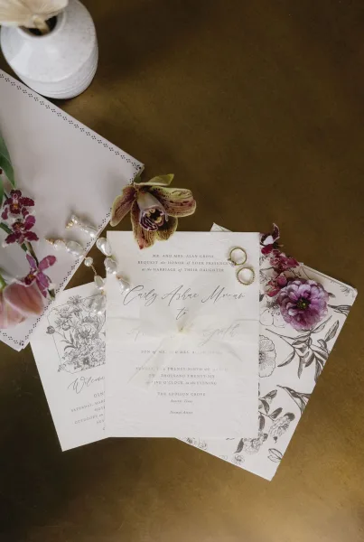 Wedding invitation suite with a floral wedding invitation artfully styled with a ribbon on a brass tabletop.