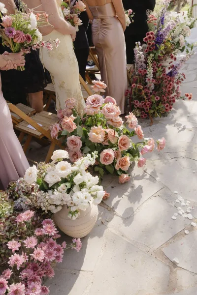 Ceremony aisle flowers line the stone walkway as ground floral arrangements frame wooden chairs in an outdoor garden.