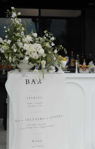 Wedding bar setup showcasing bar menu signage with a white linen banner, arranged neatly on the bar counter.