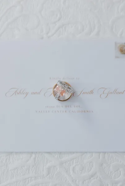Wedding ring flatlay featuring an engagement ring close up on a calligraphy envelope over textured white fabric.