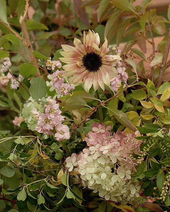 Wedding florals featuring a sunflower wedding bouquet with hydrangea, soft pink blooms, and greenery against a lush foliage backdrop
