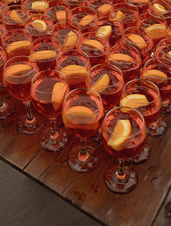 Wedding signature drink in signature cocktail glasses with aperitif cocktail, ice, and orange slices on a rustic wood table