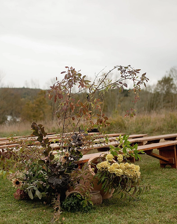 Ceremony aisle decor with outdoor ceremony aisle flowers beside wood benches, featuring hydrangeas and greenery in terracotta pots on a meadow lawn