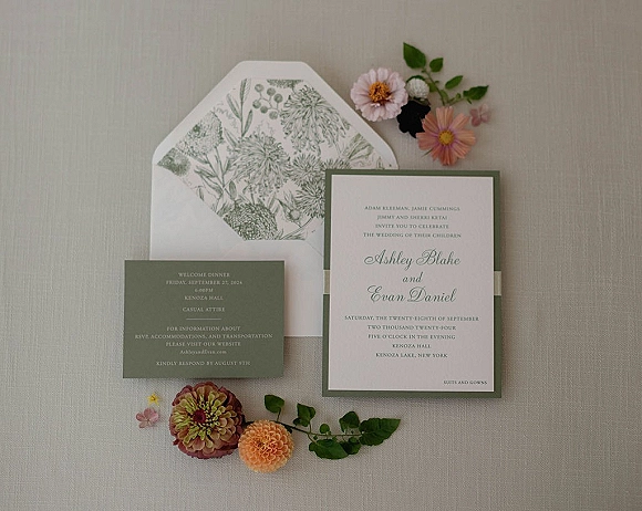 Invitation suite wedding invitation flat lay with botanical envelope liner, cards, and greenery arranged on soft linen fabric background