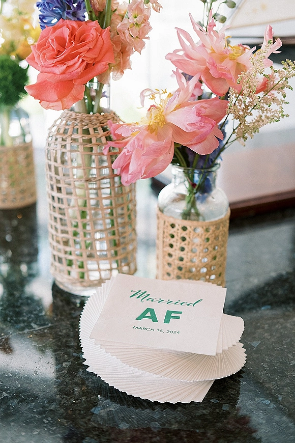 Wedding cocktail napkins stacked as custom wedding napkins with green ink monogram, styled with rattan vases and pink florals on stone countertop