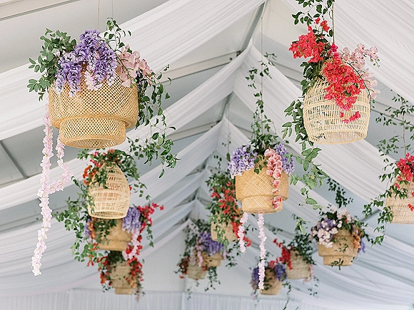 Hanging floral decor with rattan hanging basket flowers, cascading blooms and greenery garlands suspended beneath white tent drapery