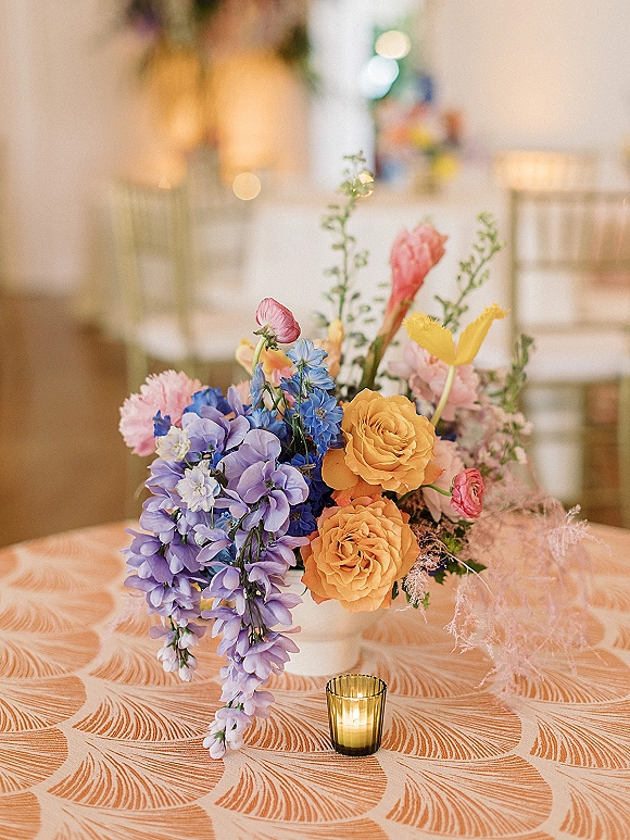 Wedding centerpiece with a colorful wedding centerpiece of bright blooms in a ceramic vase beside a gold votive candle on a patterned tablecloth