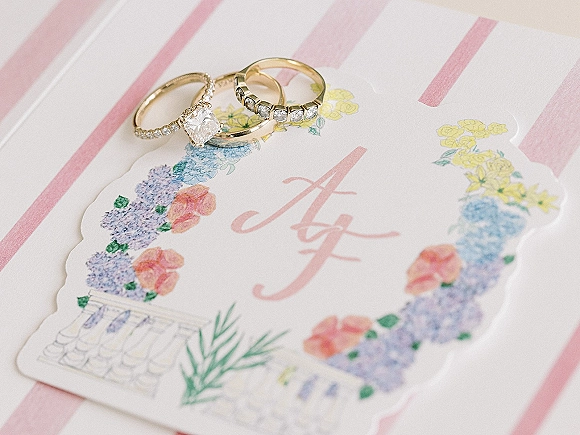 Wedding rings ring stack with diamond engagement ring and gold band resting on monogrammed scalloped stationery over striped paper surface