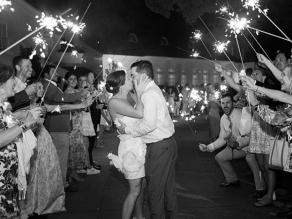Wedding send off with a sparkler exit wedding kiss as guests form a glowing tunnel in an outdoor courtyard under the night sky