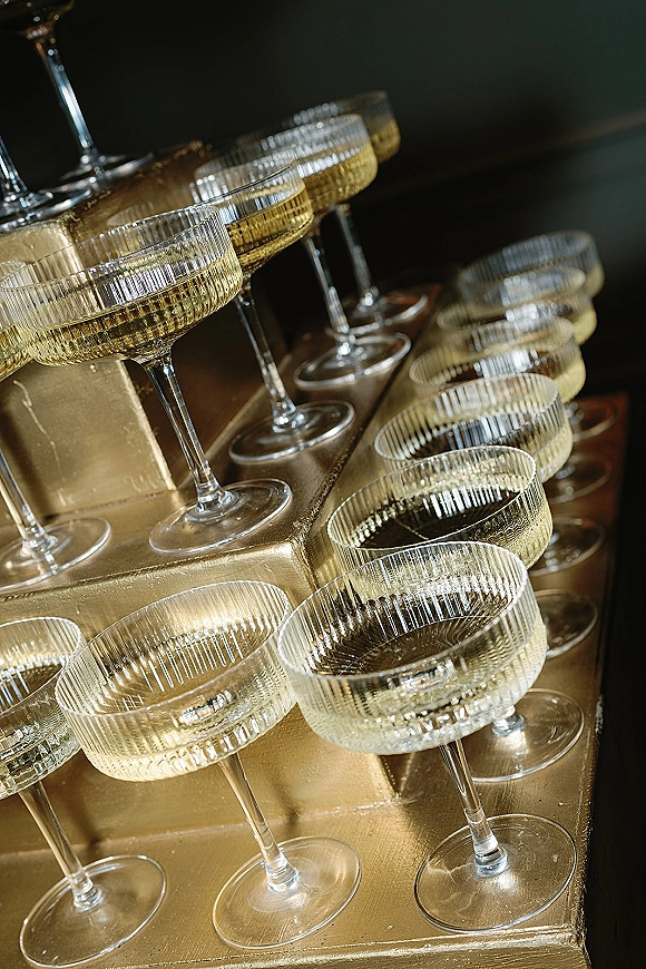 Champagne coupe tower with champagne tower setup on gold pedestal risers, stacked ribbed coupe glasses gleaming against a dark backdrop