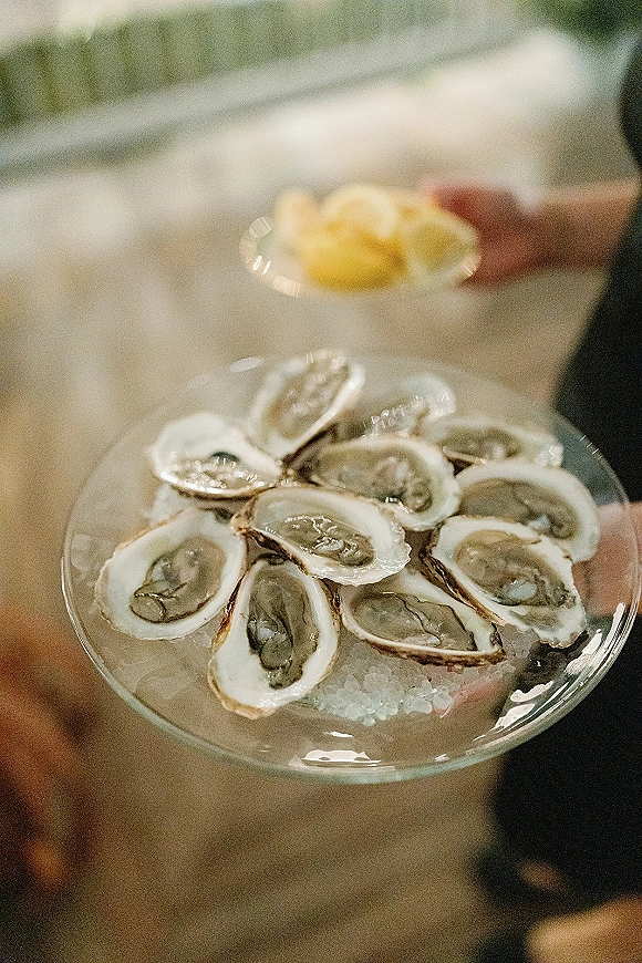 Oyster platter at an oyster bar wedding on a glass tray with oysters on crushed ice and lemon wedges, held outdoors amid greenery