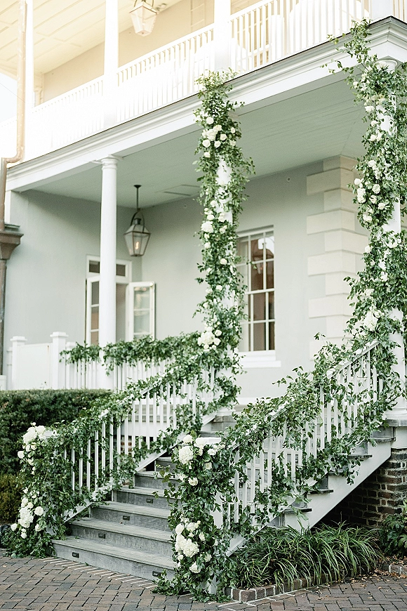 Wedding entrance decor with greenery staircase garland and white rose hydrangea swags on a porch staircase with lanterns and columns