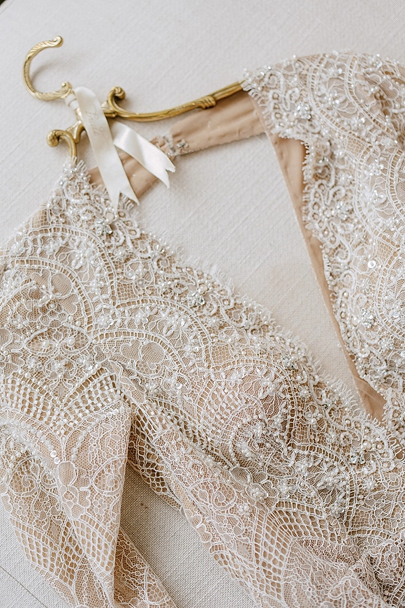 Wedding dress detail featuring lace wedding dress beading and pearls with a satin ribbon on a hanger, laid on a light fabric surface