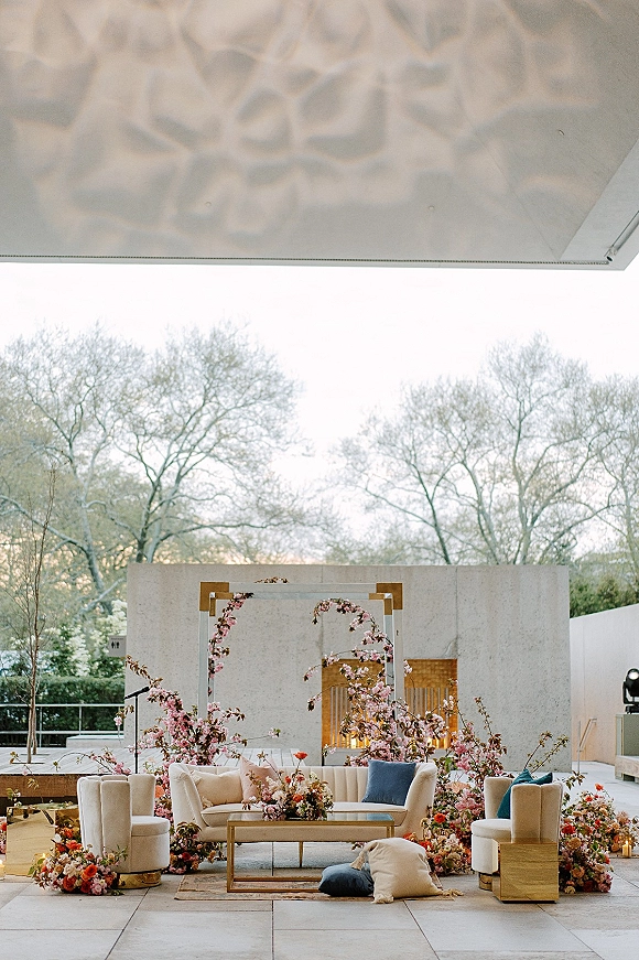 Wedding lounge decor with cream sofa, upholstered chairs and coffee table, accented by lanterns and cherry blossom branches on an outdoor patio
