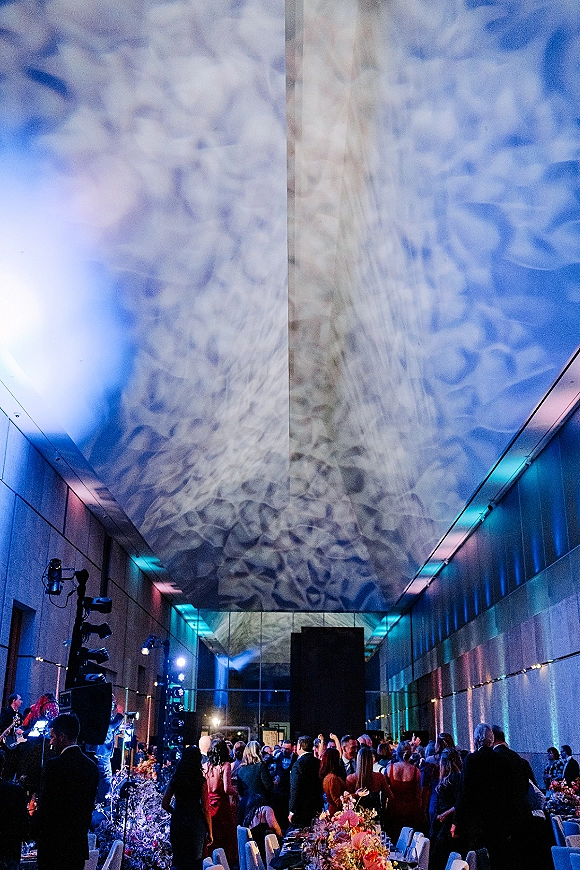 Wedding reception with wedding dance floor lighting, banquet tables and band setup in a modern event hall with ceiling projections